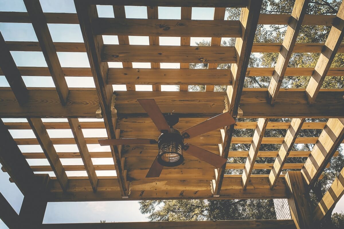 ceiling fan hanging from wooden outdoor pergola