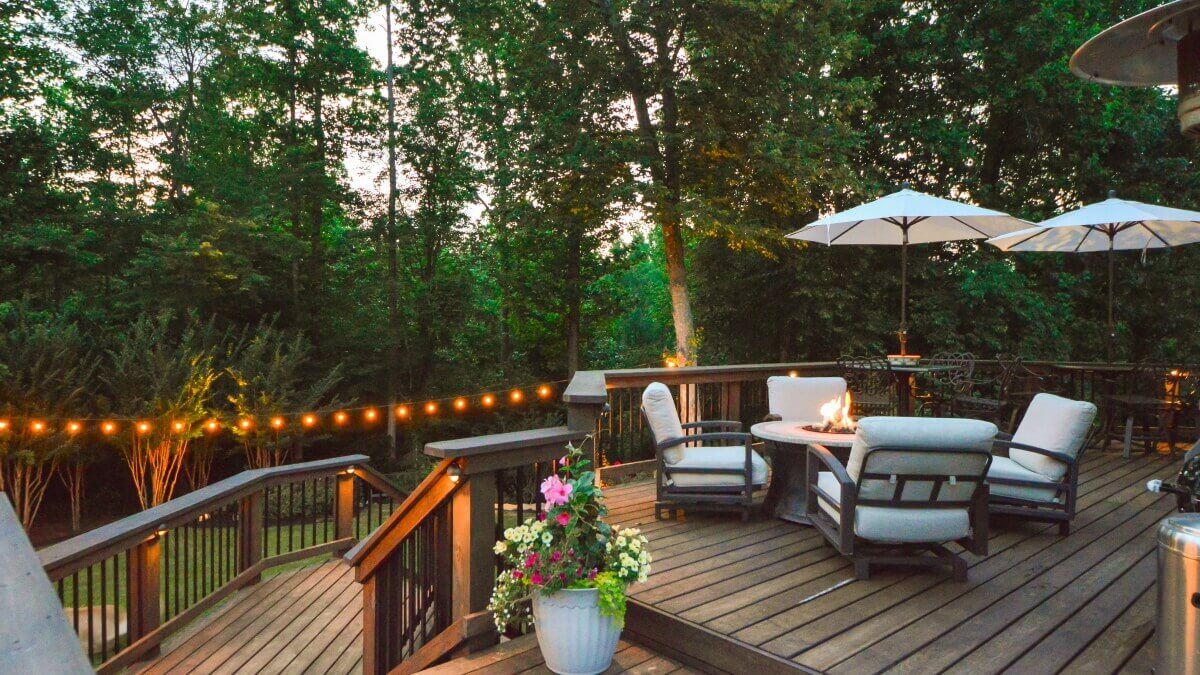 outdoor living space with fire pit, cushioned outdoor chairs, umbrellas, and outdoor hanging string lights