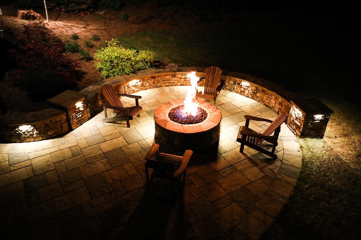 fire pit with wooden chairs and surface hardscape lighting at night
