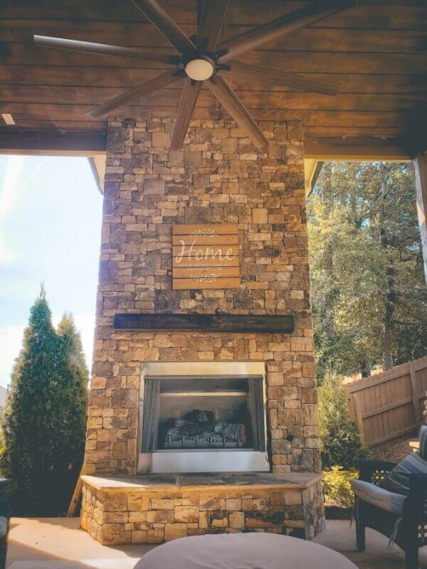 large ceiling fan above stone fire place in outdoor living room