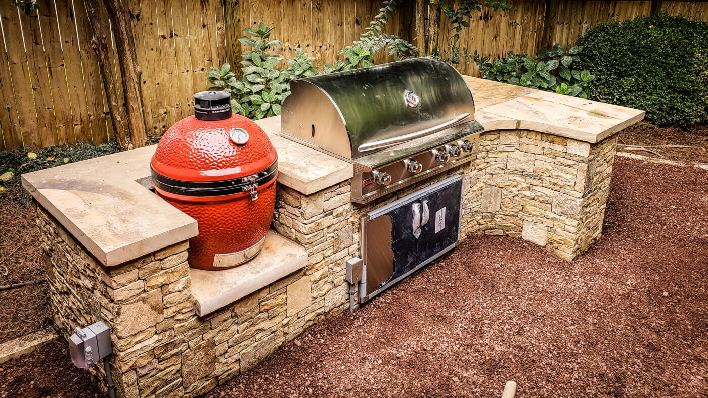 stainless steel grill and red smoker in outdoor stone kitchen