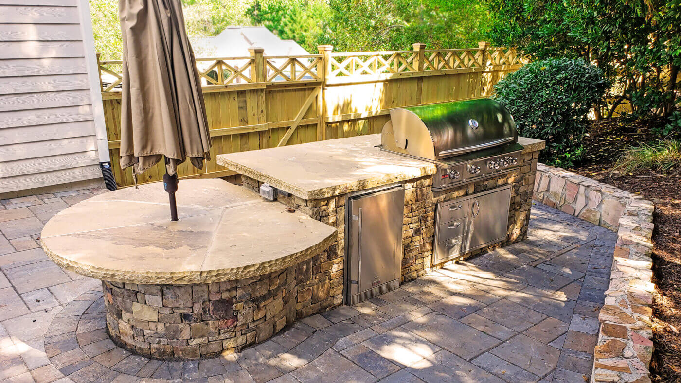 stone outdoor kitchen with steel grill and wooden privacy fence
