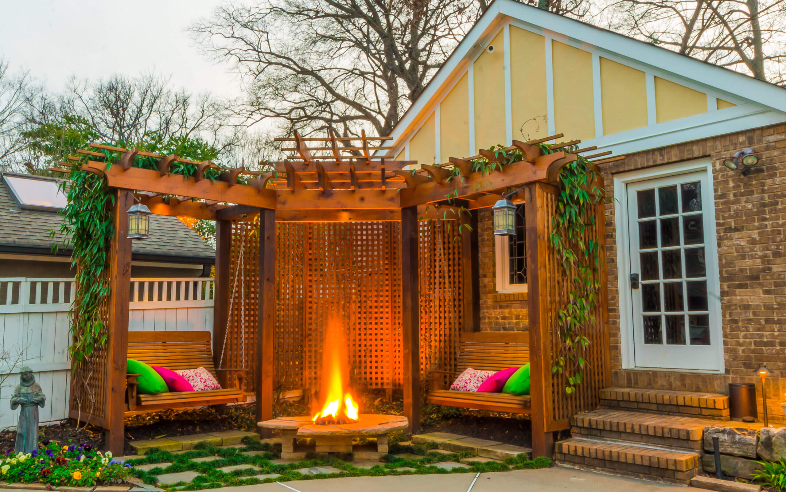 fire pit under pergola with wooden swings next to backyard guest house