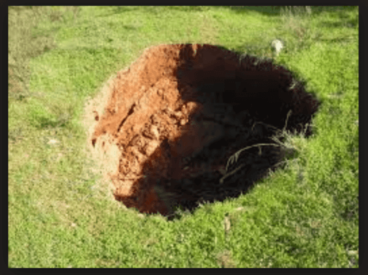 large sinkhole in middle of grass yard