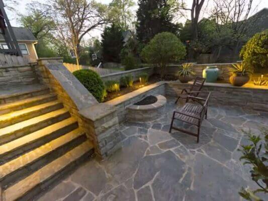 backyard stone stairway leading to outdoor patio with chairs and landscape lighting